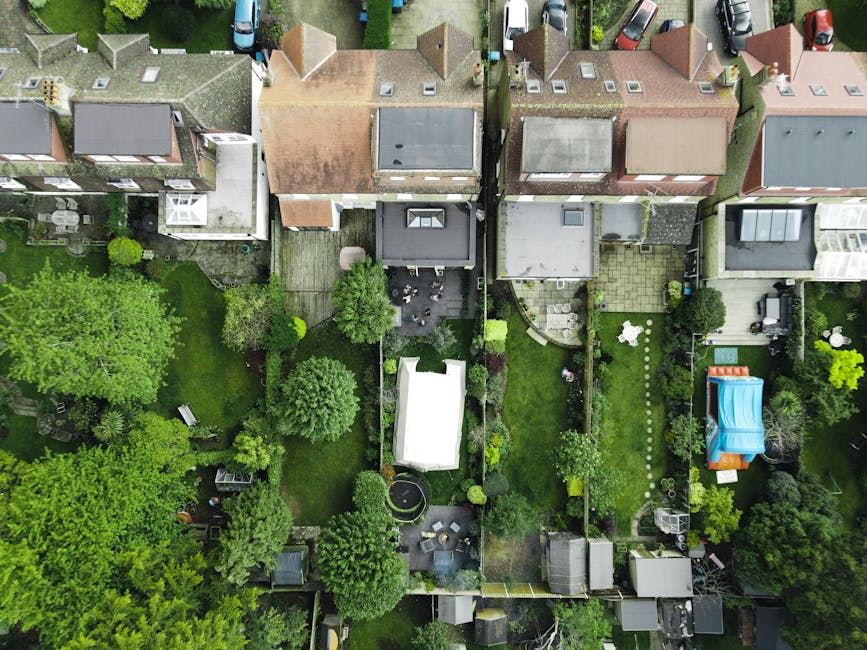 An aerial view of closely spaced residential back gardens displaying various landscaping features. From left to right, the gardens show lush green lawns with freshly mowed grass, flower beds bordered 
